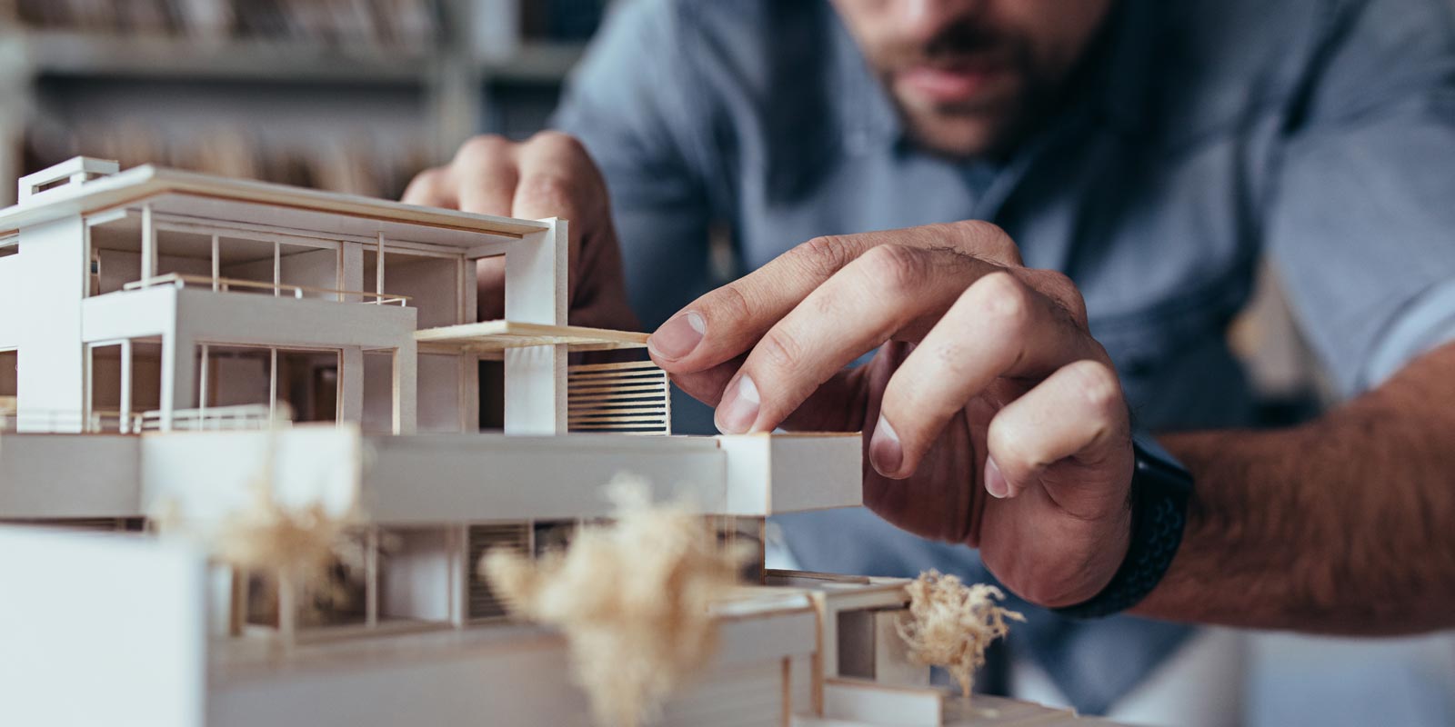 Nahaufnahme eine Architekturmodells eine Hauses. Eine Hand platziert vorsichtig ein Kleinteil