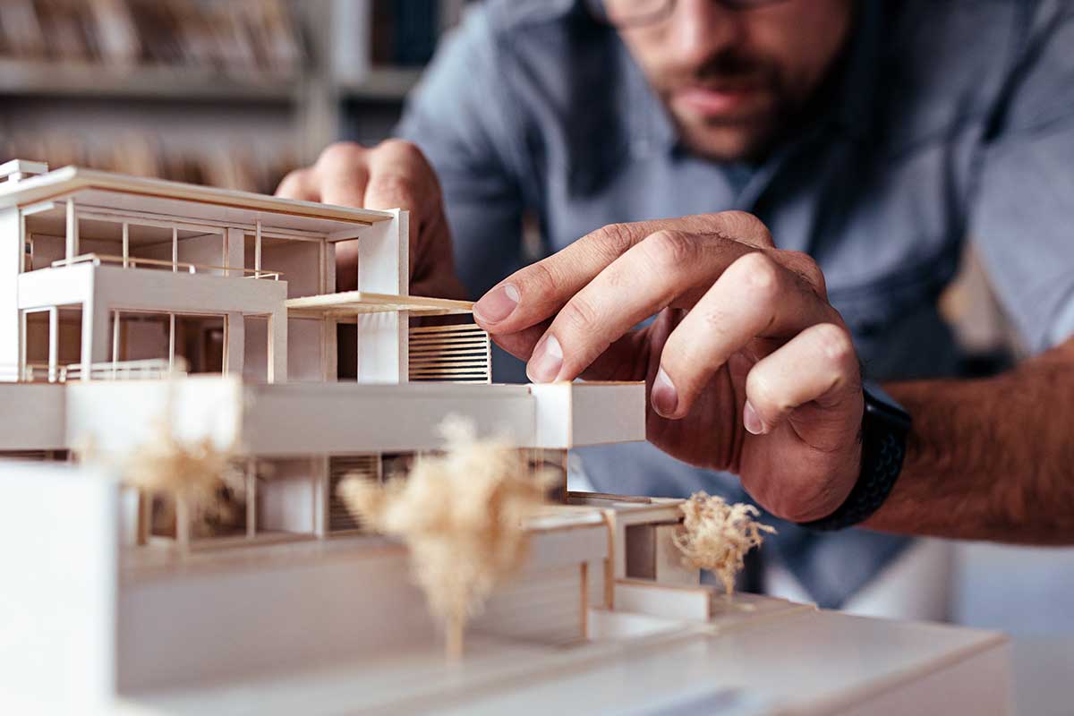 Mann betrachtet konzentriert ein Architekturmodell in einem Büro mit Bücherregalen.